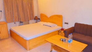 A room with a bed, a wooden nightstand, a brown sofa, and a small table with bottles.