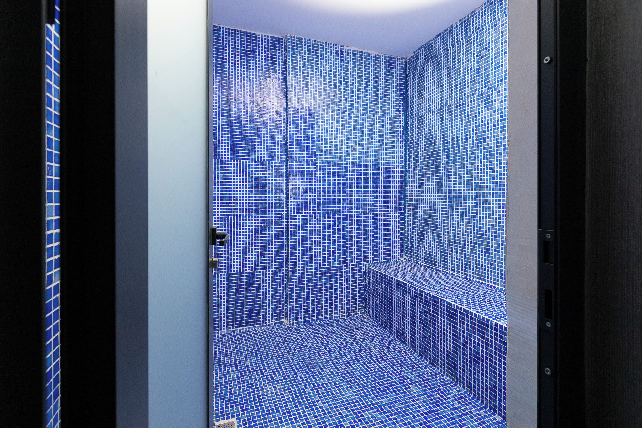 Une salle de bain avec des carreaux de mosaïque bleus, une porte et un banc.