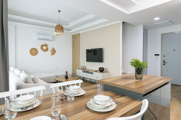Un comedor moderno con una mesa de madera dispuesta para cuatro personas, un sofá y una televisión en la pared.