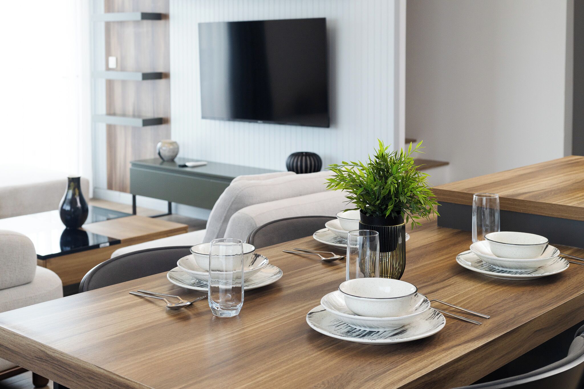 A dining table set with plates, glasses, and cutlery, a potted plant, and a flat-screen TV mounted on the wall.