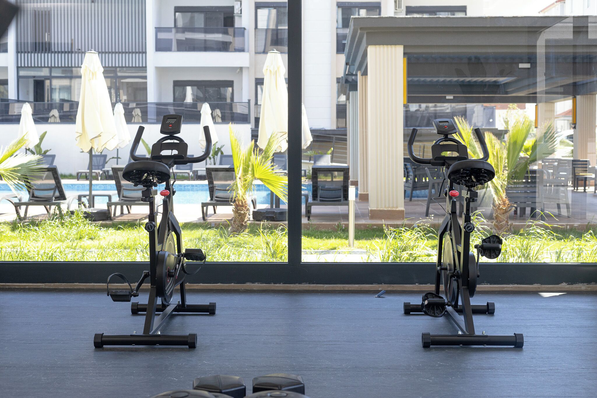 Two stationary bikes in a room with large windows overlooking a pool area.