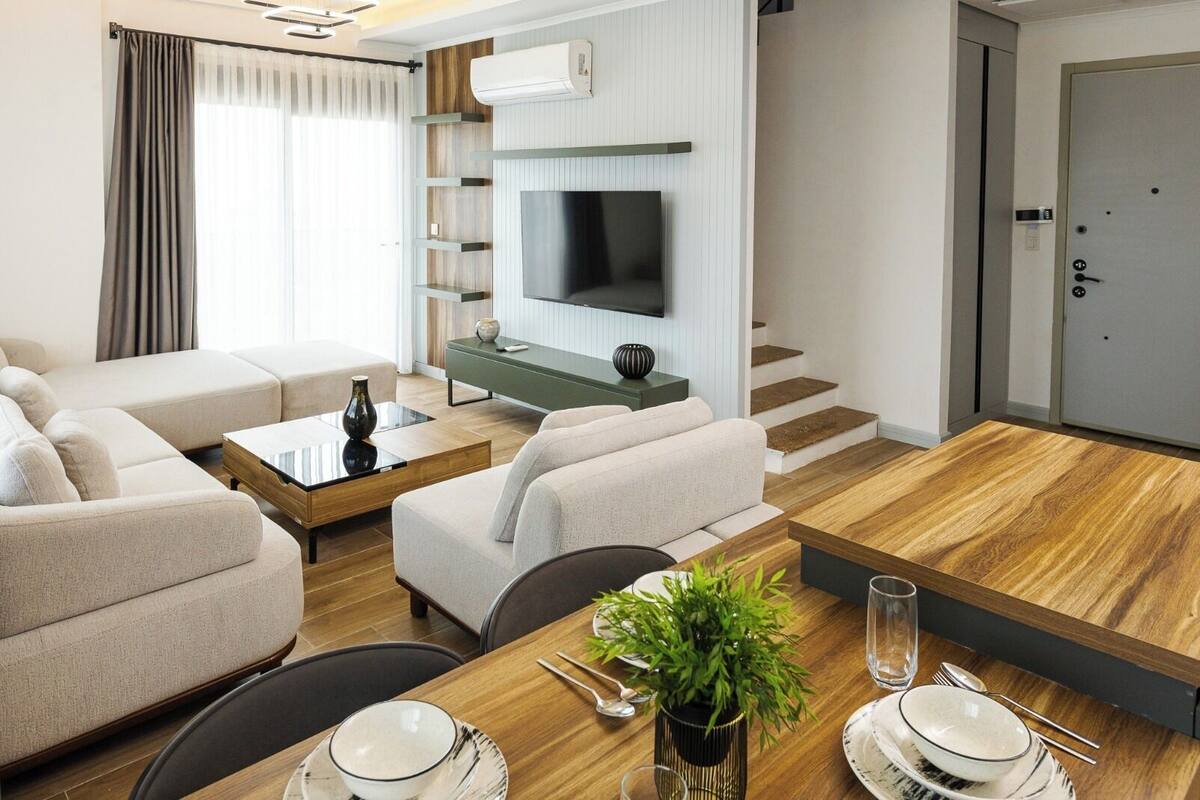 Une chambre d’hôtel moderne équipée d’un canapé, d’une table à manger pour deux personnes, d’un téléviseur et d’un escalier.