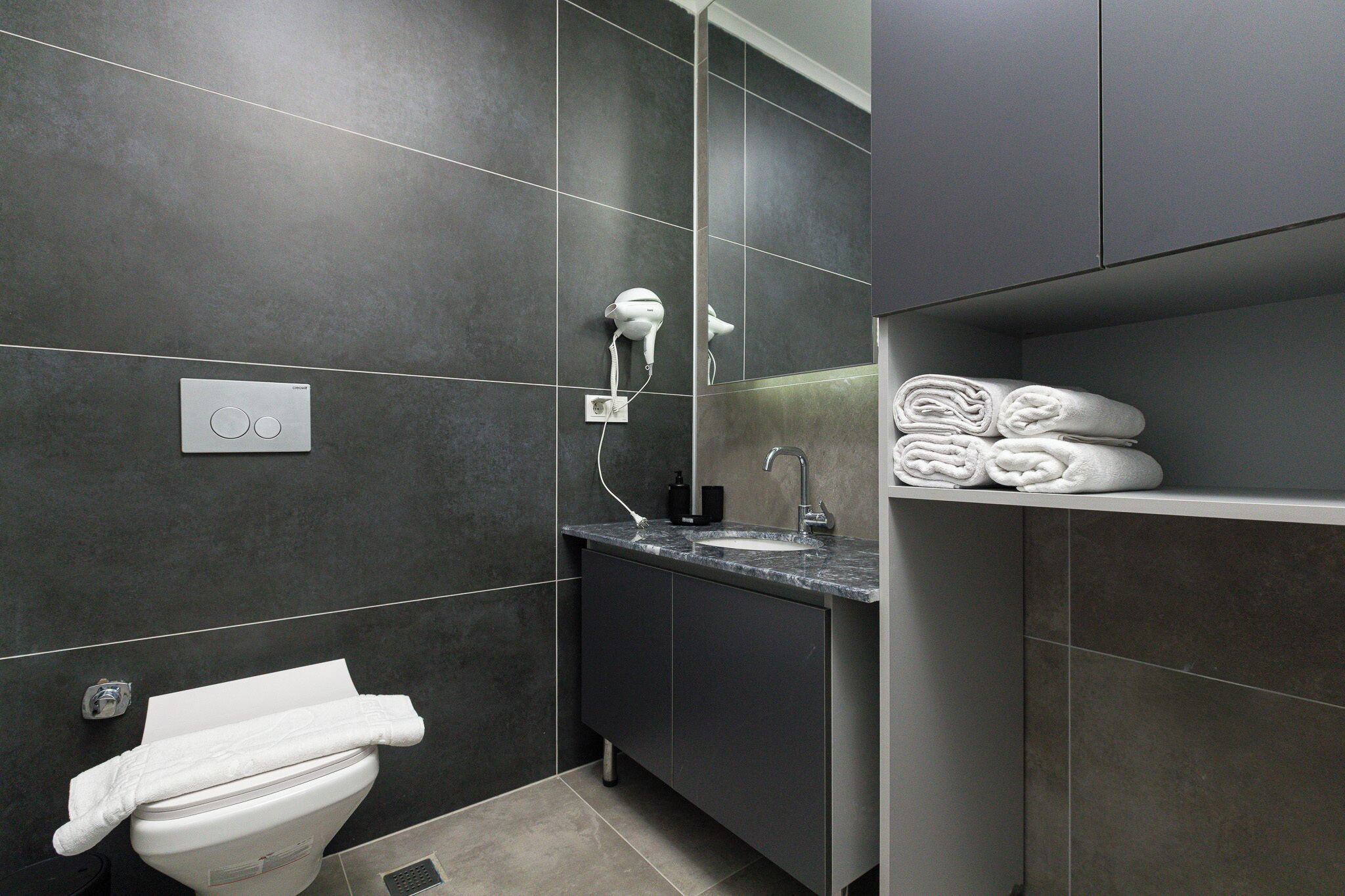 A modern bathroom with a toilet, sink, towel rack, and a mirror.
