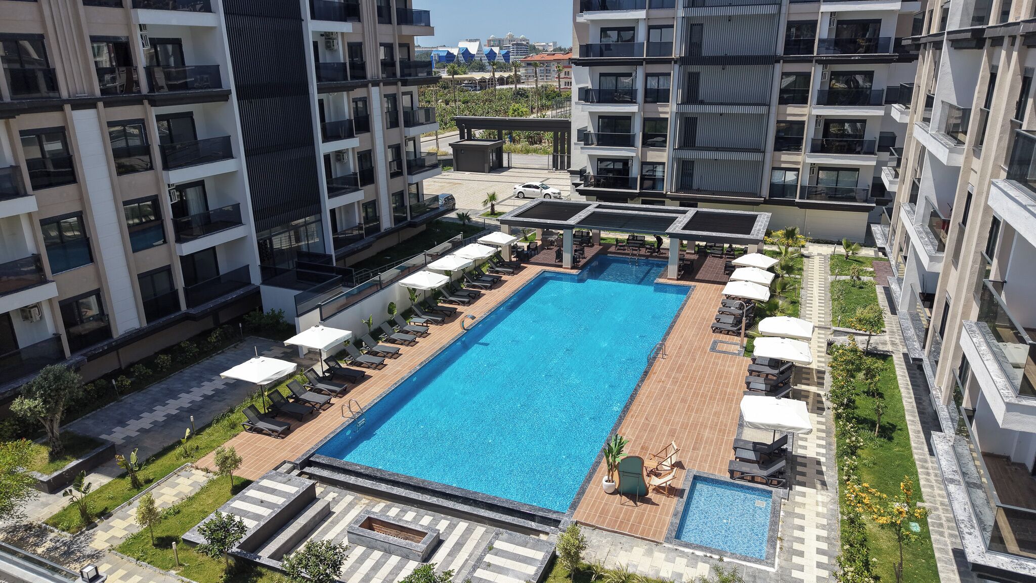 A rooftop swimming pool surrounded by lounge chairs and umbrellas, with high-rise buildings in the background.
