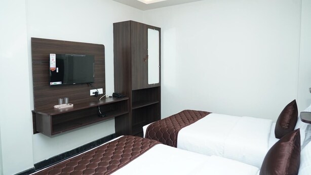 A hotel room with two beds, a TV mounted on the wall, a wardrobe, and a small shelf with a mirror and a phone.