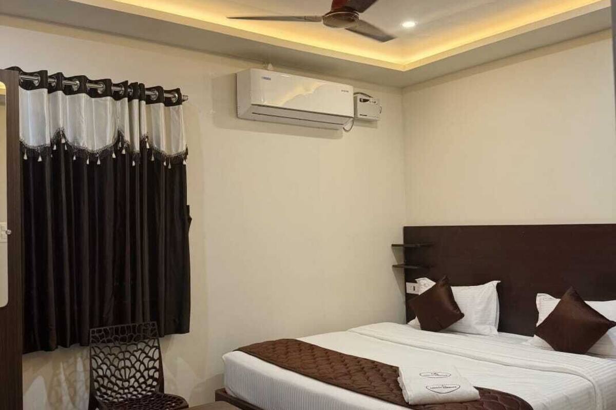 Una habitación de hotel con cama, ventilador de techo, aire acondicionado, una silla y una mesita.