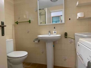 Un baño con inodoro, lavamanos, espejo y toallero.