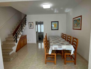Un comedor con mesa y sillas, una escalera y un pasillo que conduce a otra habitación.