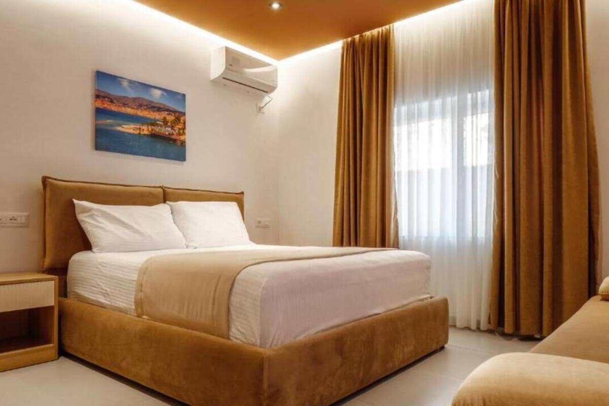 A bedroom with a bed, bedside tables, a painting, and a window with curtains.