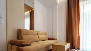 Un saló modern amb un sofà i una taula de centre, grans finestres amb cortines i il·luminació encastrada al sostre.