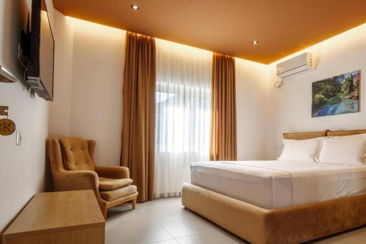 A hotel room with a bed, a chair, a TV, and a painting on the wall.