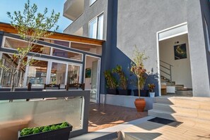 A modern building with a patio area, outdoor seating, and potted plants. - KRONOS Hotel Sarande (Sarande)