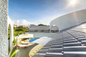 A modern building with a curved roof, a swimming pool, and lounge chairs.