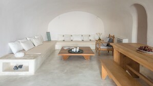 A minimalist living space with a sofa, coffee table, wooden bench, and a dining table. - Cycladica Santorini (Oia)