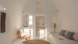 A minimalist living room with a sofa, a chair, a round rug, and a bookshelf. - Cycladica Santorini (Oia)