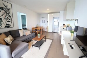 A modern living room with a sofa, coffee table, and dining area. - Beautiful Harbour View Apartment + Free Car Park (Melbourne)