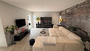 A modern living room with a large sofa, a flat-screen TV, a bookshelf, and a decorative wall. - Villa 5 minutes from the beach and Les Sables d'Olonne (Talmont-Saint-Hilaire)