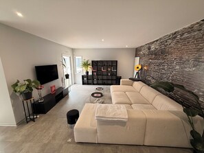 A modern living room with a large sofa, a flat-screen TV, a bookshelf, and a decorative wall. - Villa 5 minutes from the beach and Les Sables d'Olonne (Talmont-Saint-Hilaire)