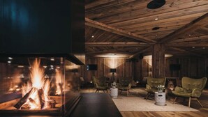 A cozy room with a fireplace, wooden walls, and comfortable seating. - VAYA Post Montafon (Gaschurn)