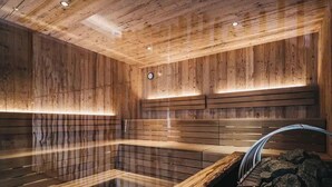 A sauna with wooden walls and benches, a clock, and a stone feature. - VAYA Post Montafon (Gaschurn)