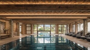 A large indoor swimming pool with wooden beams, stone walls, and a view of greenery outside. - VAYA Post Montafon (Gaschurn)