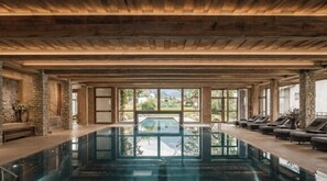 Une grande piscine intérieure avec des poutres en bois, des murs en pierre et une vue sur la verdure environnante.