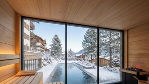 A modern sauna room with a large window overlooking a snowy landscape and a pool. - VAYA Post Montafon (Gaschurn)