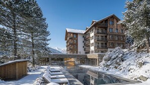 A hotel with a pool, snow-covered surroundings, and a mountain backdrop. - VAYA Post Montafon (Gaschurn)