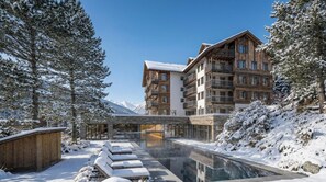 Un hotel con piscina, paisajes nevados y montañas al fondo.
