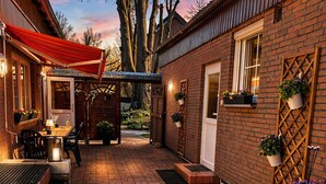 En byggnad i tegel med ett rött markis, utomhusplatser, ljusslingor och krukväxter.