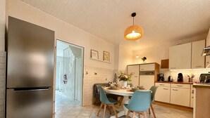 Ett modernt kök med ett kylskåp i rostfritt stål, ett matbord med stolar och en hängande lampa.