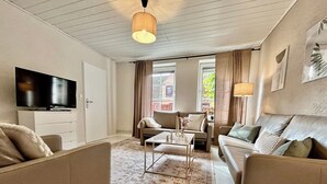 Ett modernt vardagsrum med en platt-TV, två soffor, ett soffbord och en mönstrad matta.