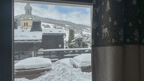 Eine verschneite Landschaft, durch ein Fenster ist ein Gebäude mit einem Glockenturm zu sehen.