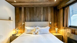 Ein Schlafzimmer mit Holzwänden, einem großen Bett, zwei Nachttischen mit Lampen und einem Fenster mit Vorhängen.