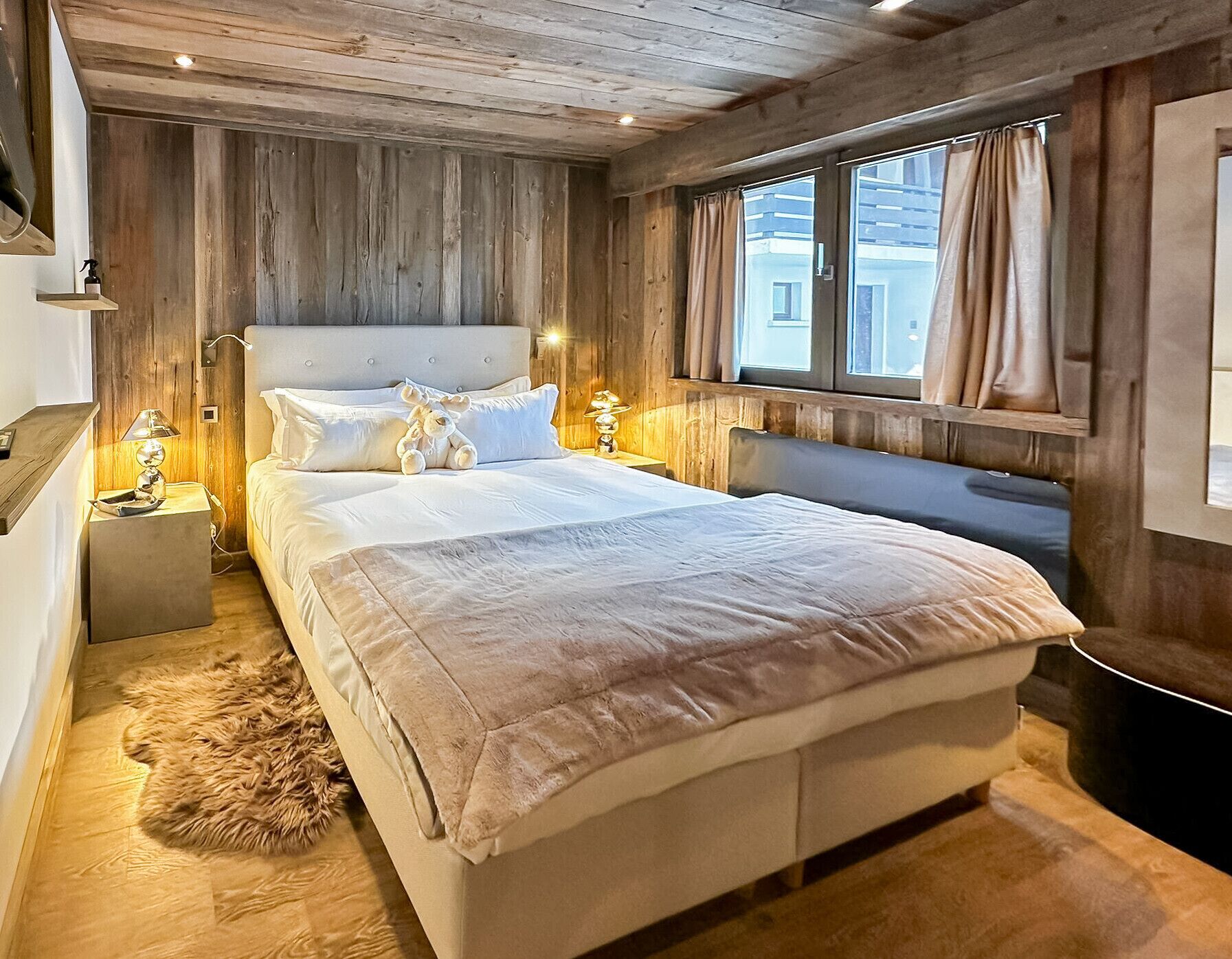 Ein Schlafzimmer mit Holzwänden, einem großen Bett, Nachttischlampen und einem Fellteppich.