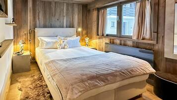 Een slaapkamer met houten lambrisering, een groot bed, bedlampjes en een vachttapijt.
