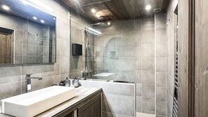 Ein modernes Badezimmer mit einem großen Spiegel, einem weißen Waschbecken, einer Duschkabine und einer Holzbeschichtung an der Decke.