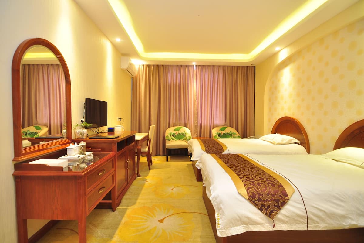 A hotel room with two beds, a desk with a TV, a mirror, and a large window with curtains.