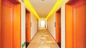 Un couloir d’hôtel avec des portes en bois, une moquette à motifs et un plafond clair.