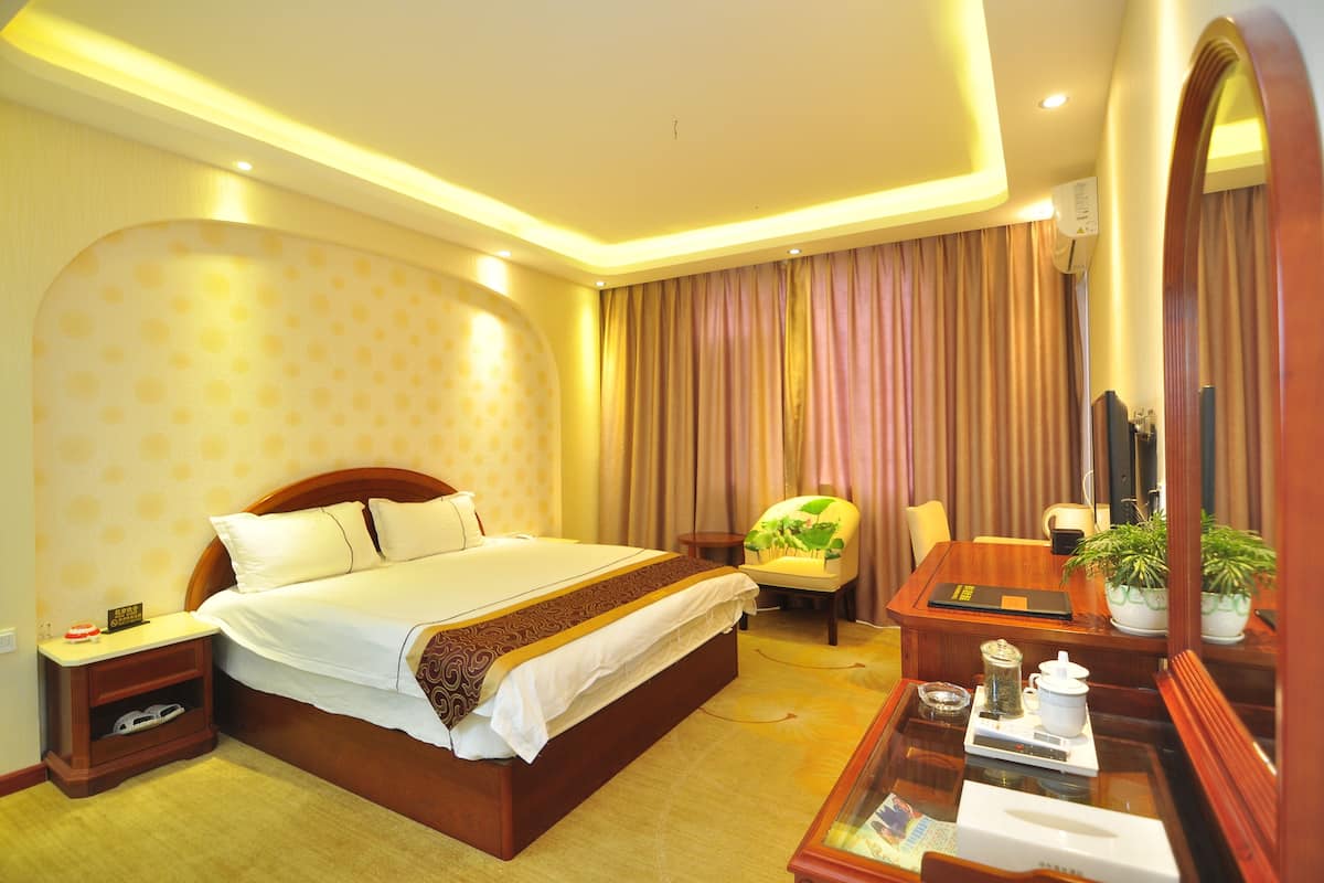 A hotel room with a bed, bedside table, chair, desk, and a mirror.