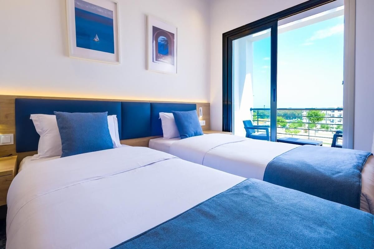 Una habitación de hotel con dos camas, un ventanal grande y obras de arte en la pared.