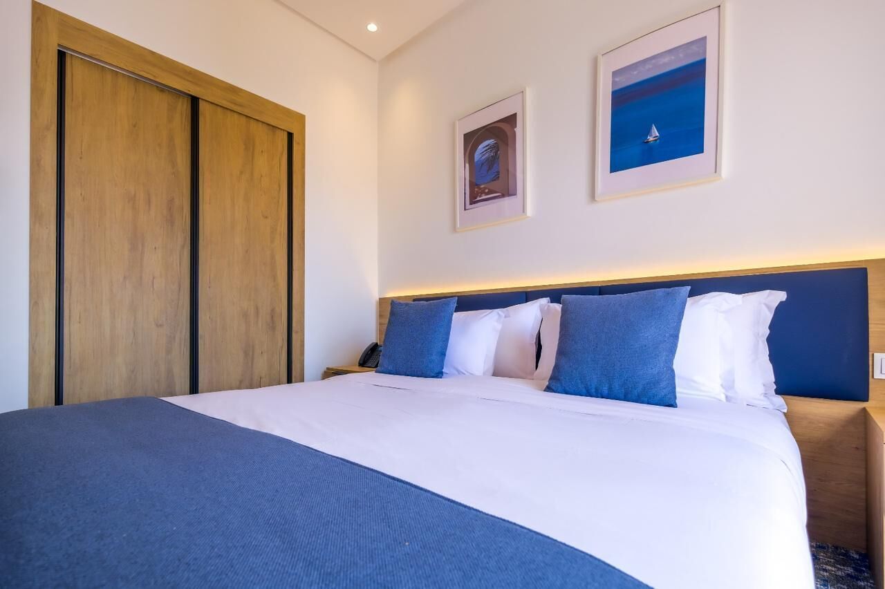 A hotel room with a bed, a wooden wardrobe, and two framed pictures on the wall.