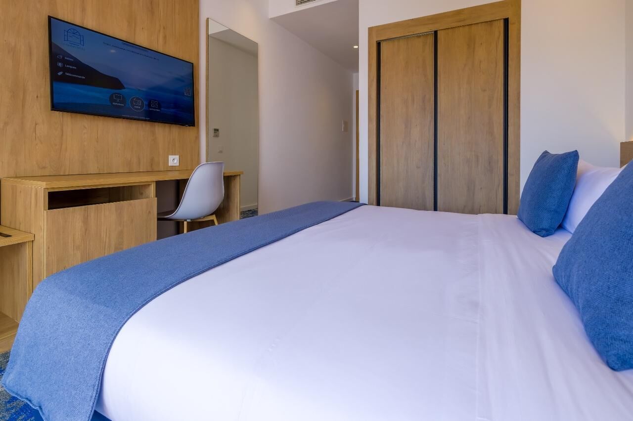 Habitación de hotel con cama, escritorio, silla, televisor montado en la pared y armario de madera.
