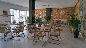 A restaurant with wicker chairs and tables, large windows, and a decorative wall with circular patterns.