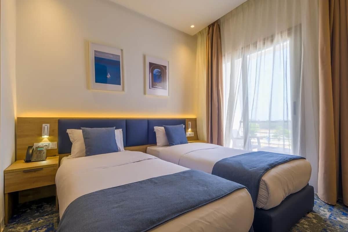 Una habitación de hotel con dos camas, una mesita de noche con teléfono y una ventana con cortinas.