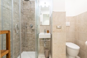 Un baño con cabina de ducha de vidrio, un lavamanos blanco y un inodoro.