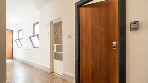 Un pasillo con una puerta de madera, un portero automático de metal y una ventana con celosía metálica.