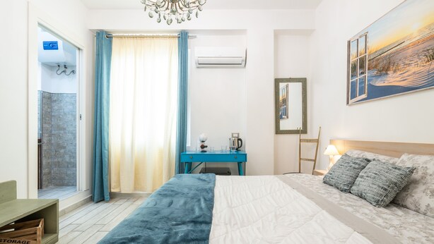 Una camera d'albergo con un letto, una scrivania, una sedia, una finestra con tende, un condizionatore d'aria e un quadro appeso al muro.