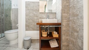 Un bagno con box doccia in vetro, un water, un lavandino con specchio sopra e una mensola in legno con asciugamani e cesti.