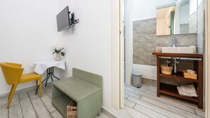 Un bagno con un mobile bagno in legno, un lavandino, uno specchio, una televisione a parete, una sedia e una panca.